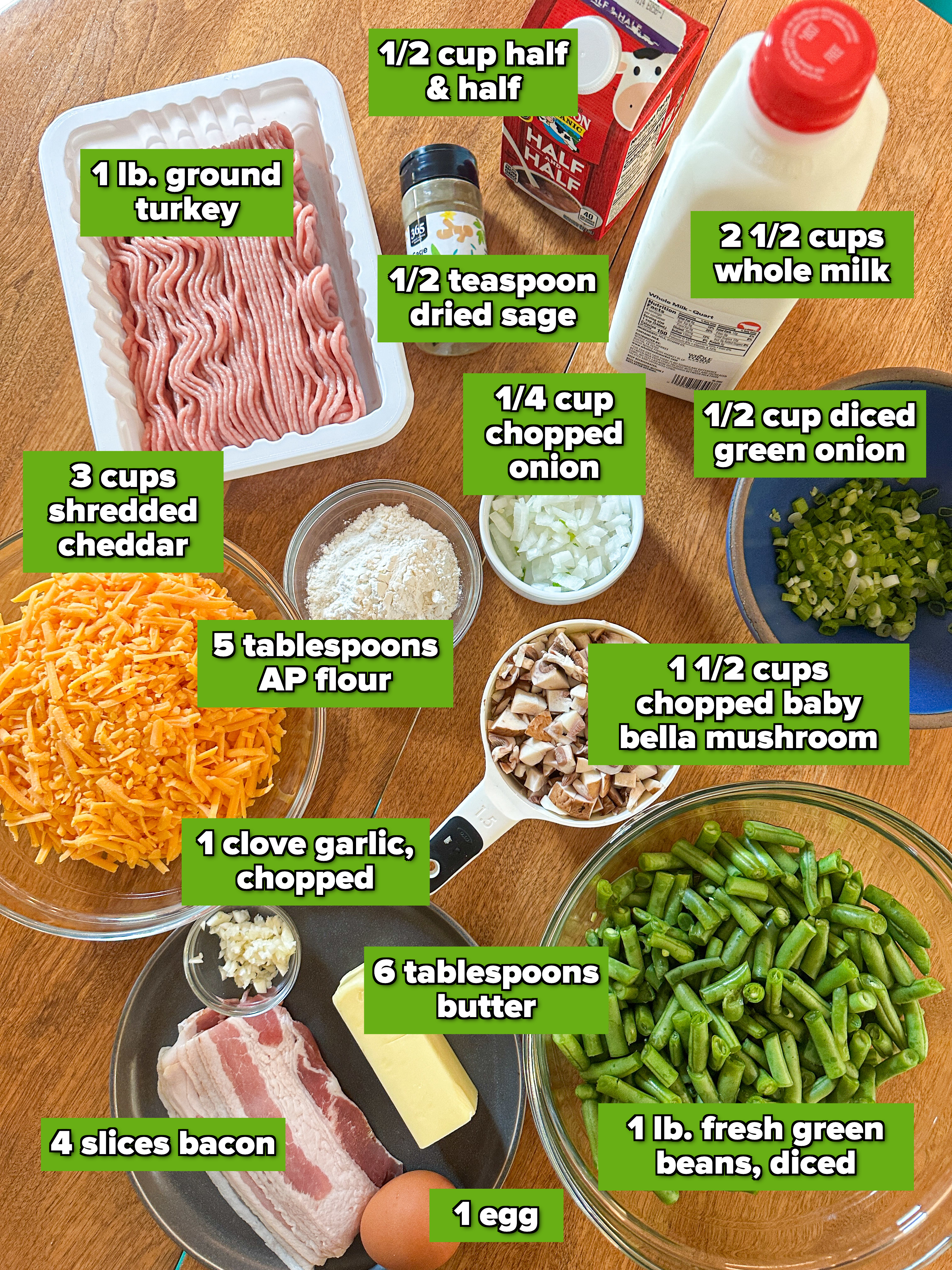 Ingredients on a table include ground meat, green beans, shredded cheese, bacon, mushrooms, spices, flour, butter, garlic, chopped onion, chopped green onions, egg, and milk