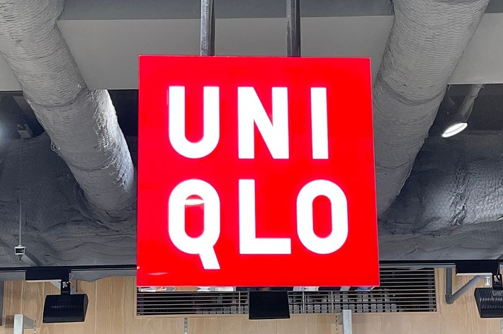 ユニクロ店舗の内部。天井から吊り下げられた赤いユニクロの看板が中央に見える。下にはディスプレイされた商品と価格が表示されている。