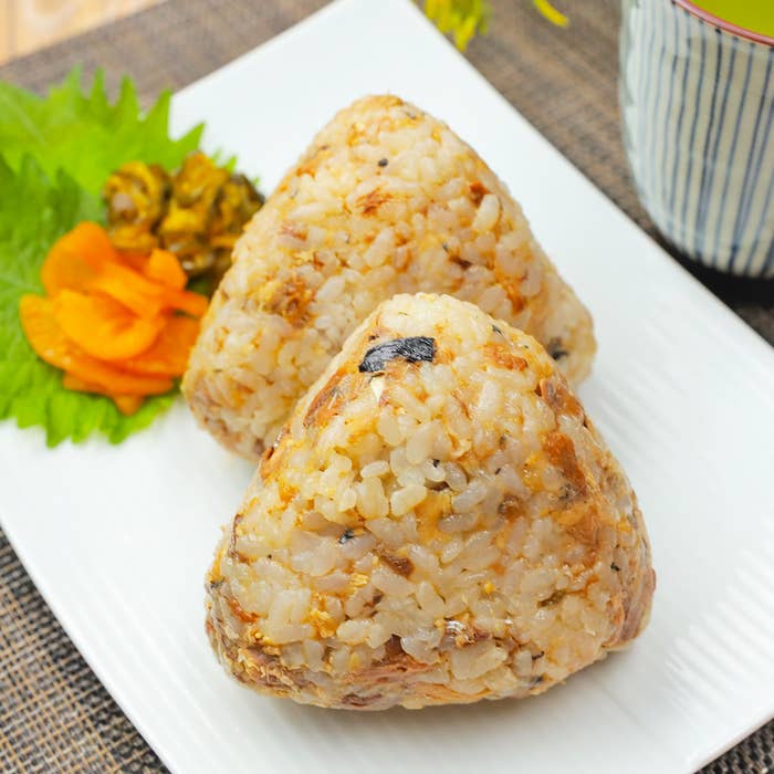 白い皿に盛られた2つの焼きおにぎり。隣には漬物の添え物がある。