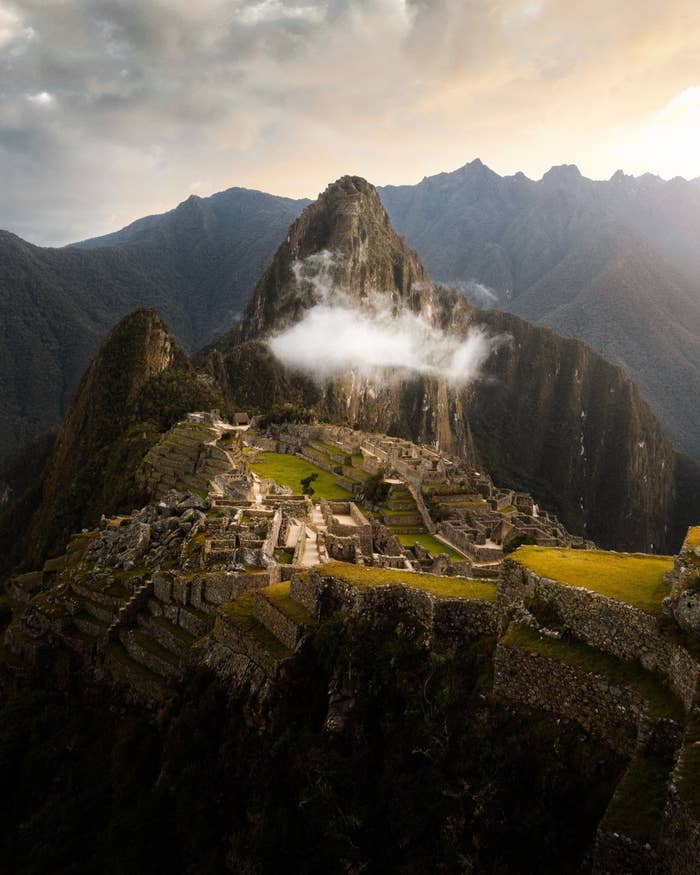 View of the historical site Machu Picchu, with steep terraced fields and ancient ruins set against a backdrop of soaring mountains and clouds