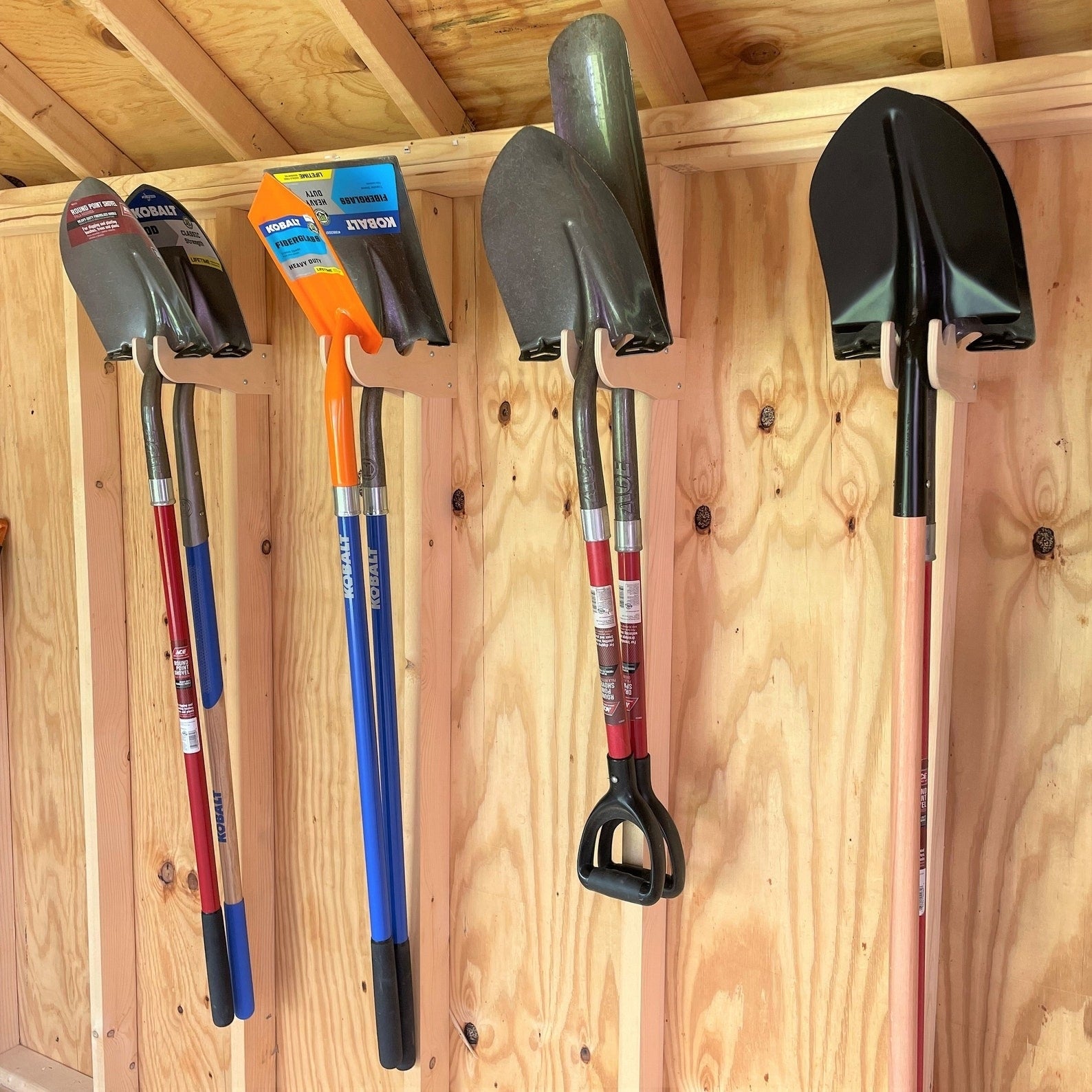 Five antithetic  types of shovels hanging connected  the woody  hooks against the partition  of a woody  shed