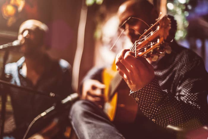 Two unidentified musicians perform with a guitar and a microphone, one singing and the other playing the guitar, in an intimate setting