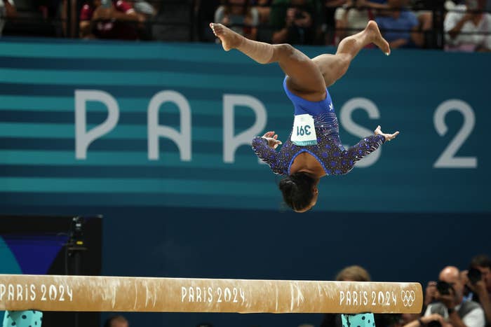 Simone Biles performs a gravity-defying flip above the balance beam at the Paris 2024 Olympics, displaying incredible athleticism and focus