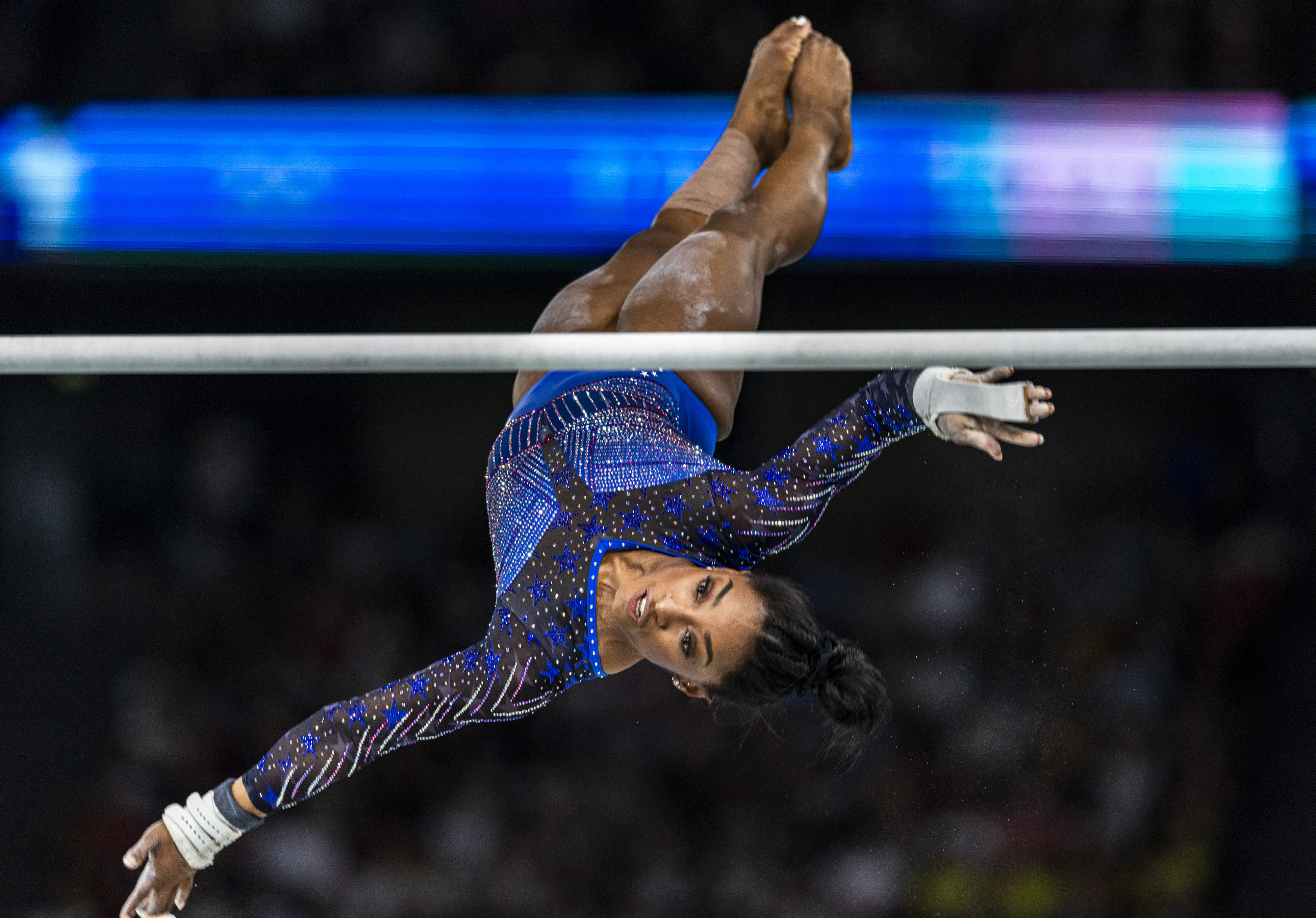 Simone Biles performs a gymnastic routine on the uneven bars, wearing a sparkling leotard