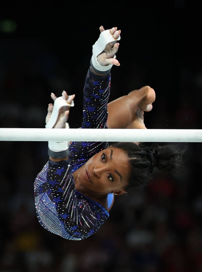 Simone Biles, in a shimmering leotard, reaches for the uneven bars during a gymnastics routine
