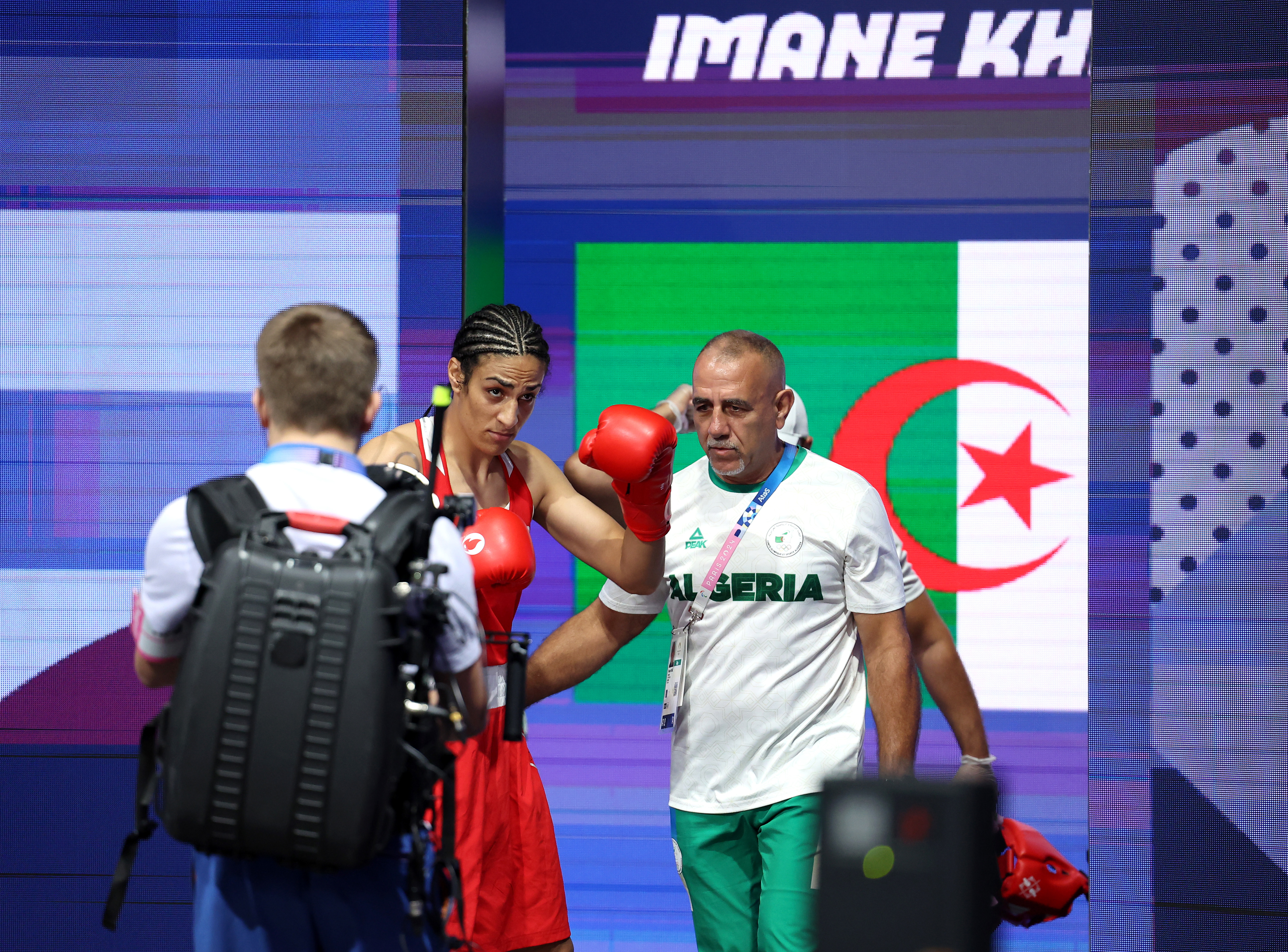 Boxer Imane Khelif, alongside her coach before a match. An Algerian flag is displayed in the background