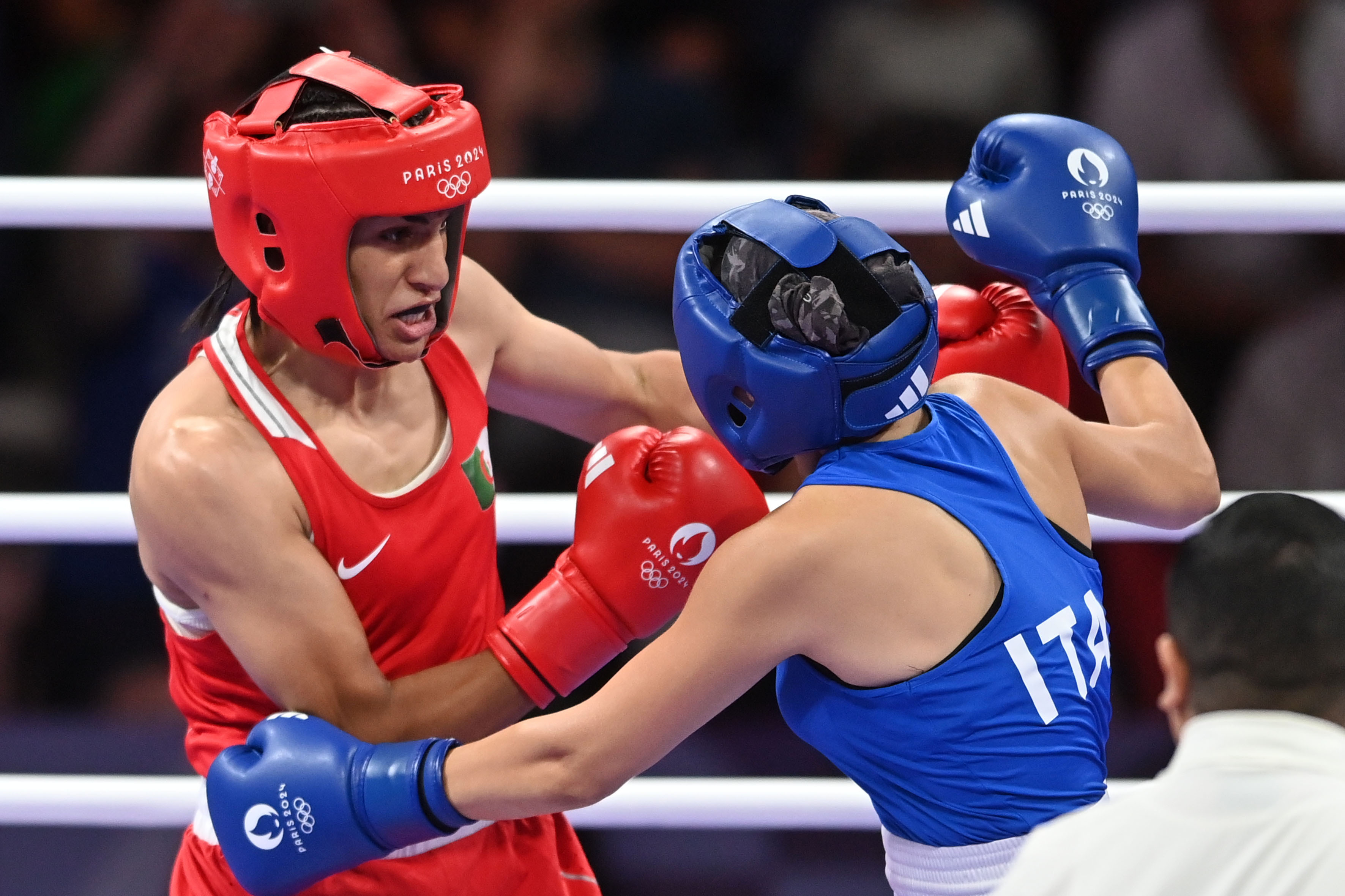 Two boxers, one in a red outfit and the other in a blue outfit, are fighting in a boxing ring during a sports event