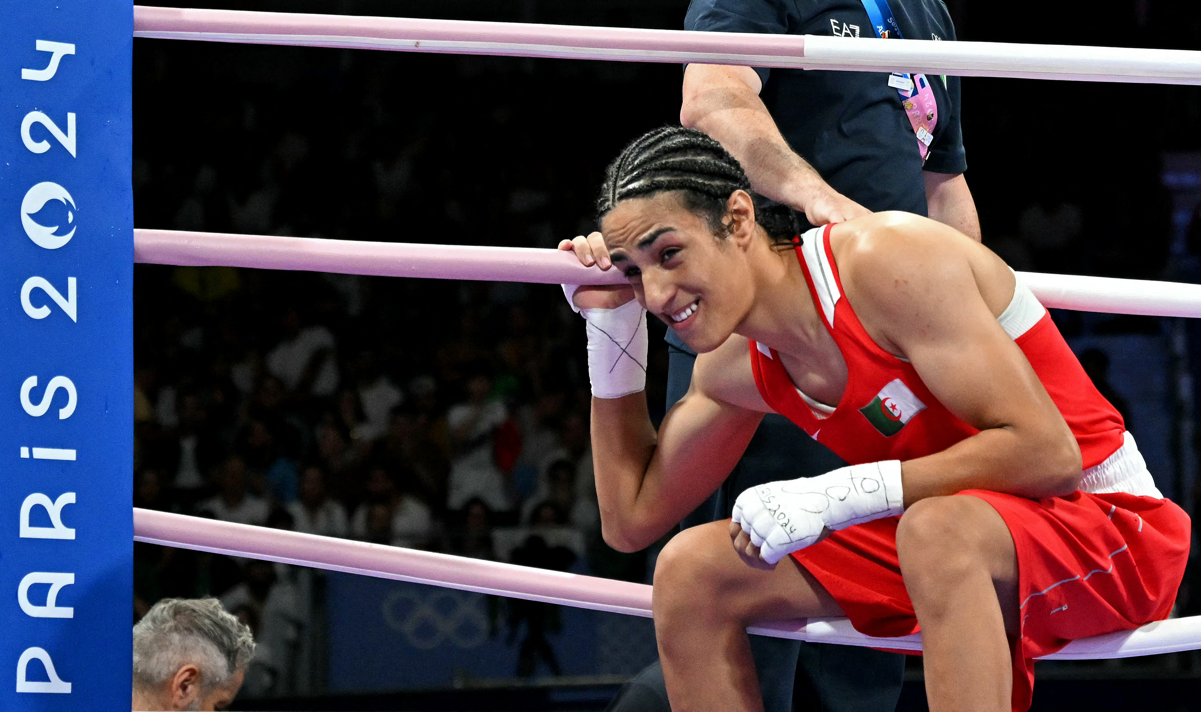 Imane sits in a corner of the boxing ring, smiling after a match. The ring has "Paris 2024" written on the post