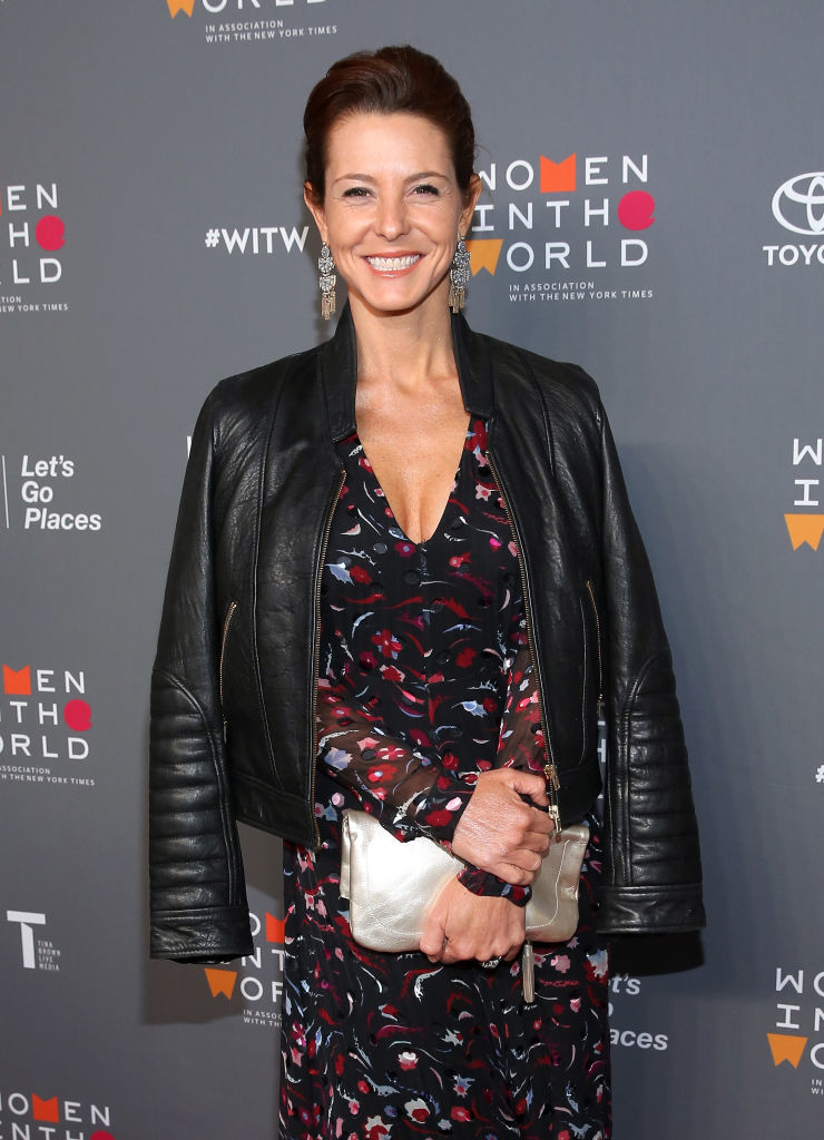 AJ wearing leather jacket over a patterned dress, holding a clutch, poses for a photo at the Women in the World event
