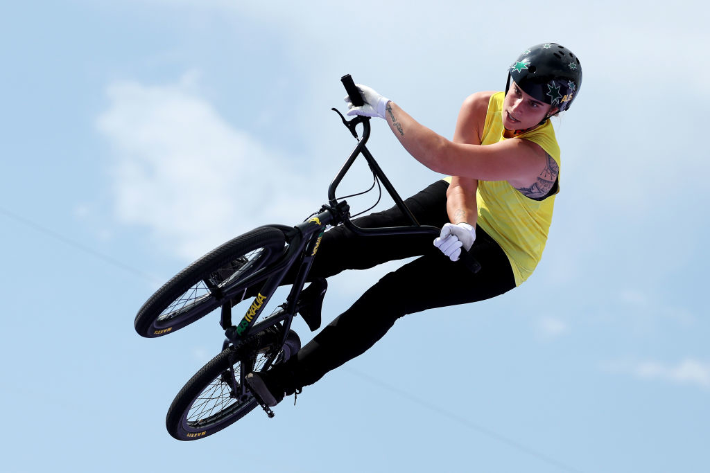A person wearing a helmet and gloves performs an aerial trick on a BMX bike against a clear sky