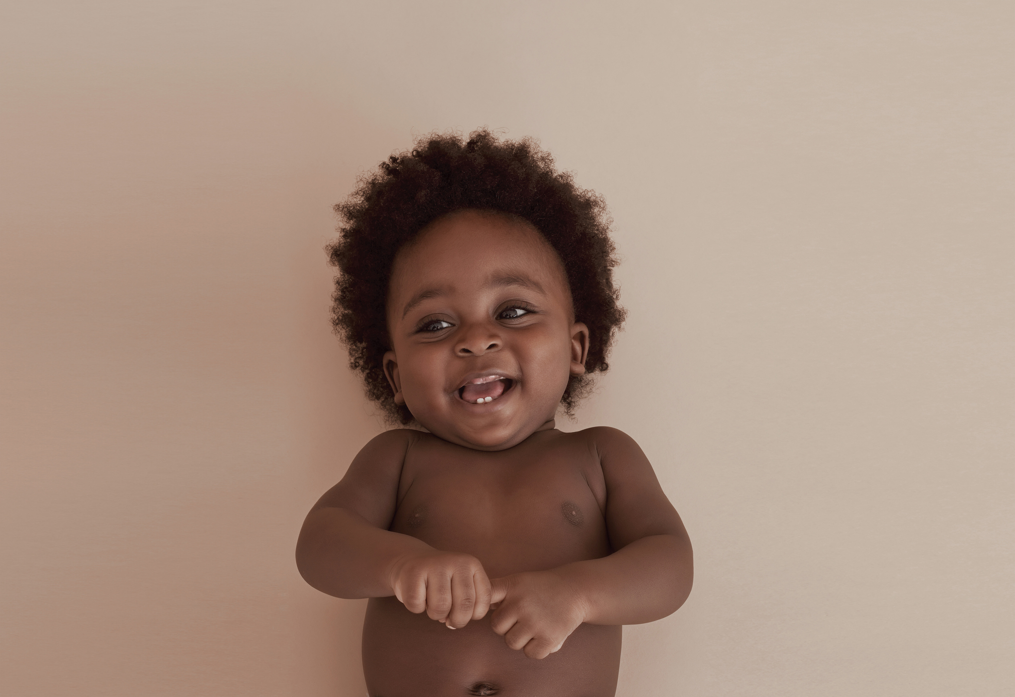 A baby with curly hair lies on their back, smiling and looking up