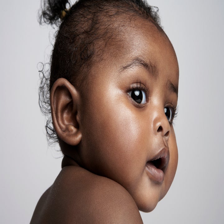 A close-up photo of a baby's face, with expressive eyes and a curious expression. The baby has short, curly hair. No other persons are in the image