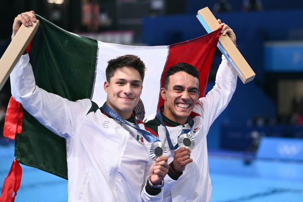 Atletas sonrientes, Kevin Berlín y Iván García, sostienen una bandera de México y muestran sus medallas ganadas en una competencia deportiva