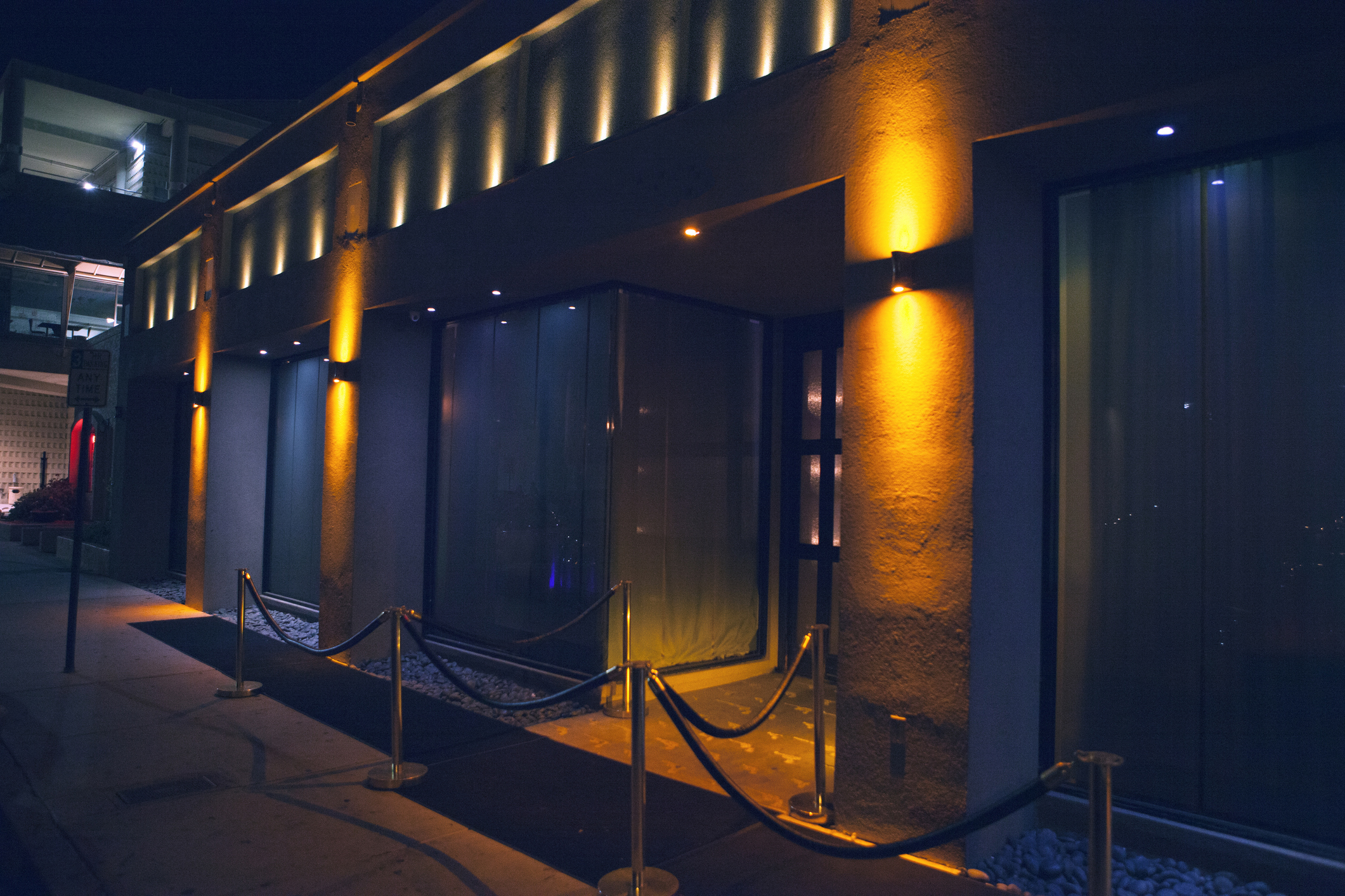 Outside view of a chic venue with illuminated architectural details and velvet rope barriers, hinting at an exclusive event or club