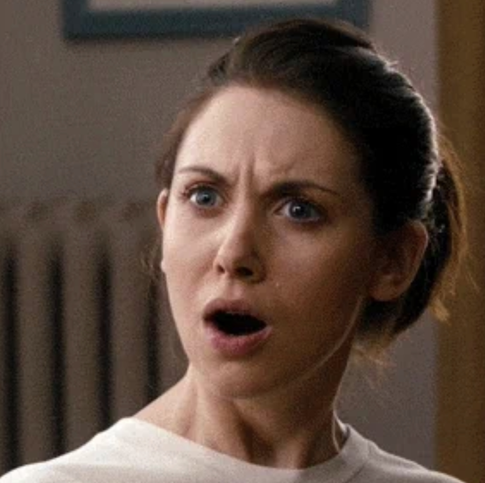 A woman with a surprised expression, eyebrows raised and mouth open, wearing a light-colored top