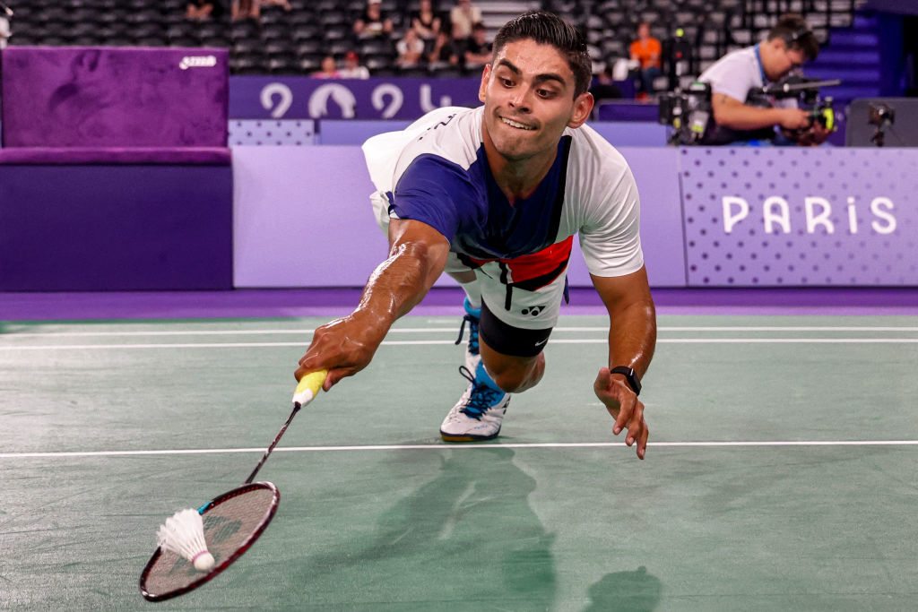 Player lunges to hit a shuttlecock during a badminton match, with "Paris" displayed in the background