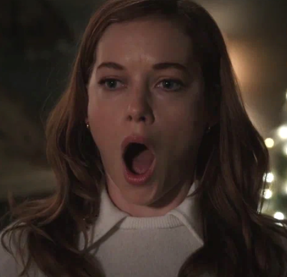 A woman with long hair and a surprised expression wears a long-sleeve top