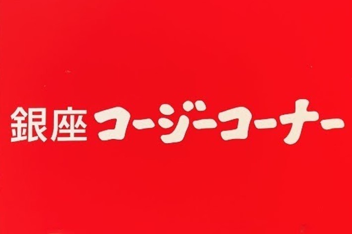 A metal sign with red and white text reads &ldquo;銀座コージーコーナー&rdquo; (Ginza Cozy Corner) on a brick wall