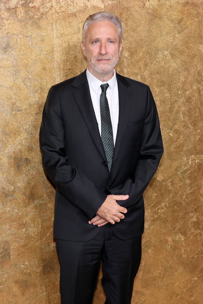 A man in a black suit and white shirt poses against a textured background