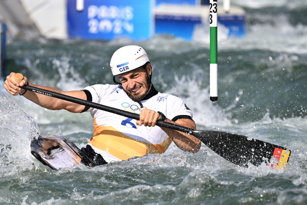 Slalom canoeist Sebastian Brendel competes in a whitewater event at Paris 2024 Olympics. He wears a protective helmet and paddles through turbulent water
