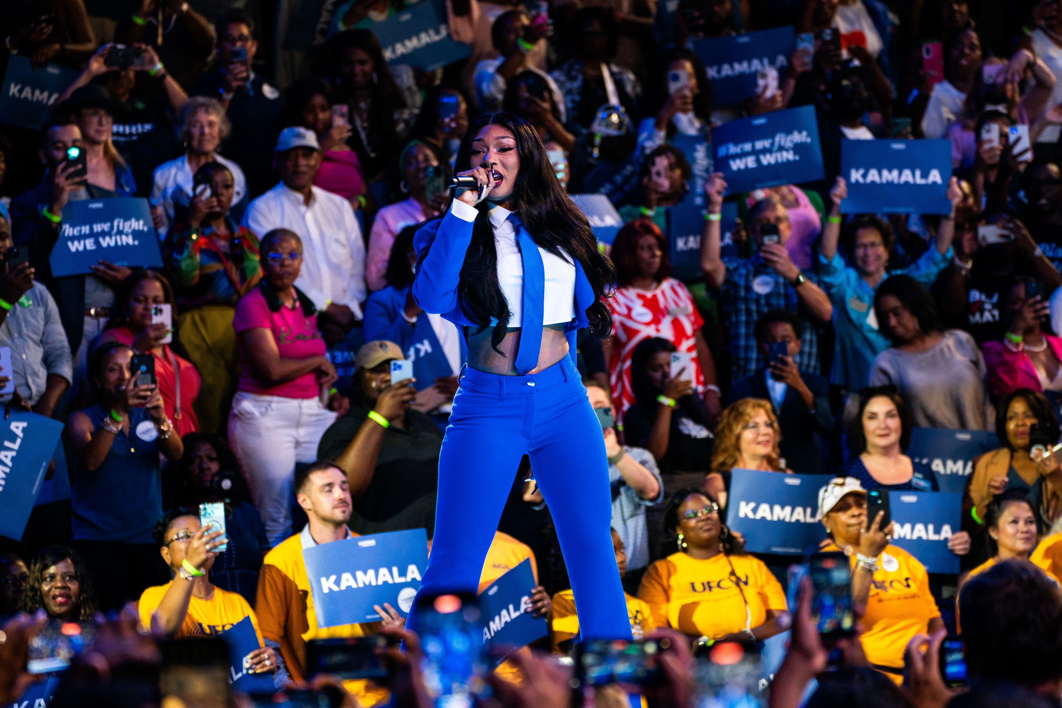 Megan Thee Stallion performs on stage at a large rally. The crowd holds blue &quot;Kamala&quot; signs, showing support for Kamala Harris