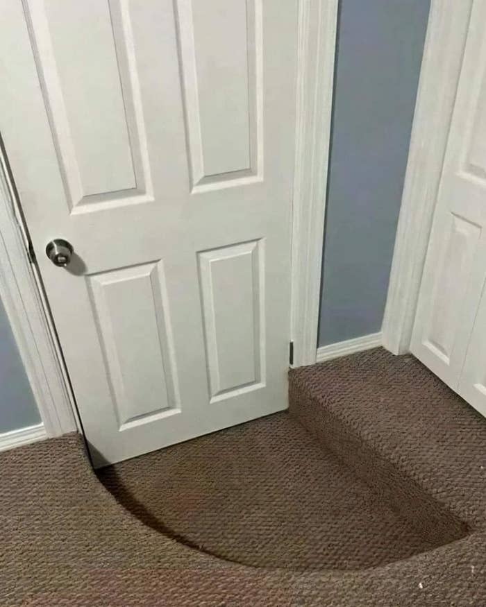 A white door with a cut-out shape at the bottom to fit over a step in the carpeted floor. The step leads to another level
