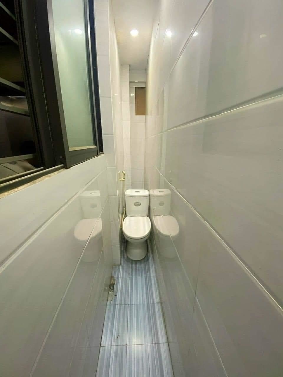 A very narrow bathroom with a toilet squeezed tightly between two walls, with just enough space to walk down a narrow path to reach it