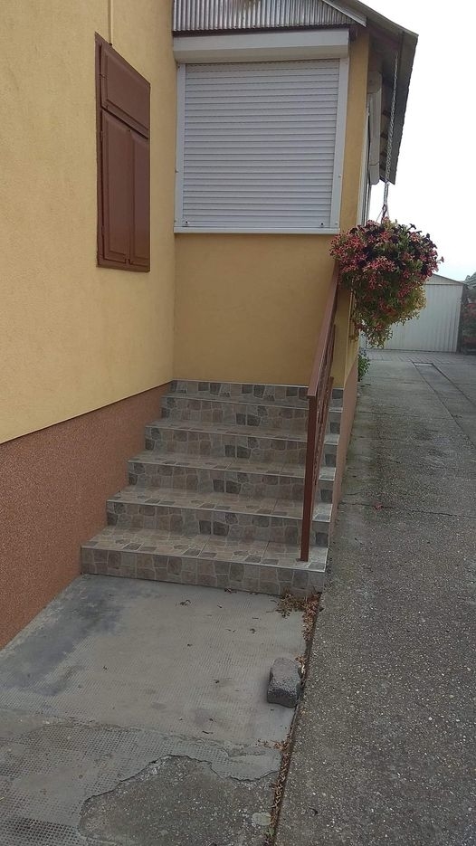 Outdoor staircase with nine tiled steps, leading to a closed door with a window shutter and a flower basket hanging from the railing