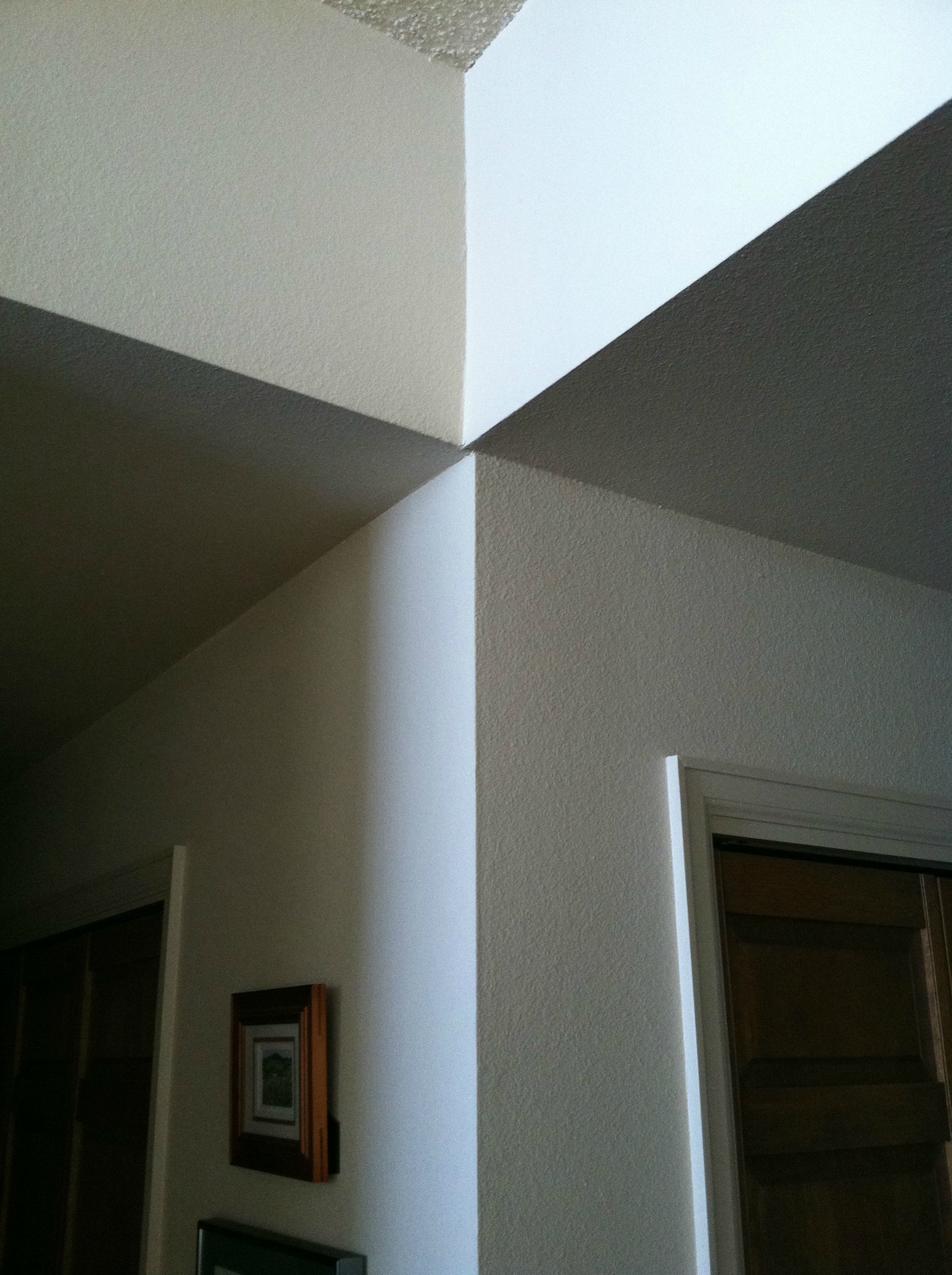 A close-up image of a corner junction of two white-colored walls and the ceiling in a house, with a small framed picture on one wall