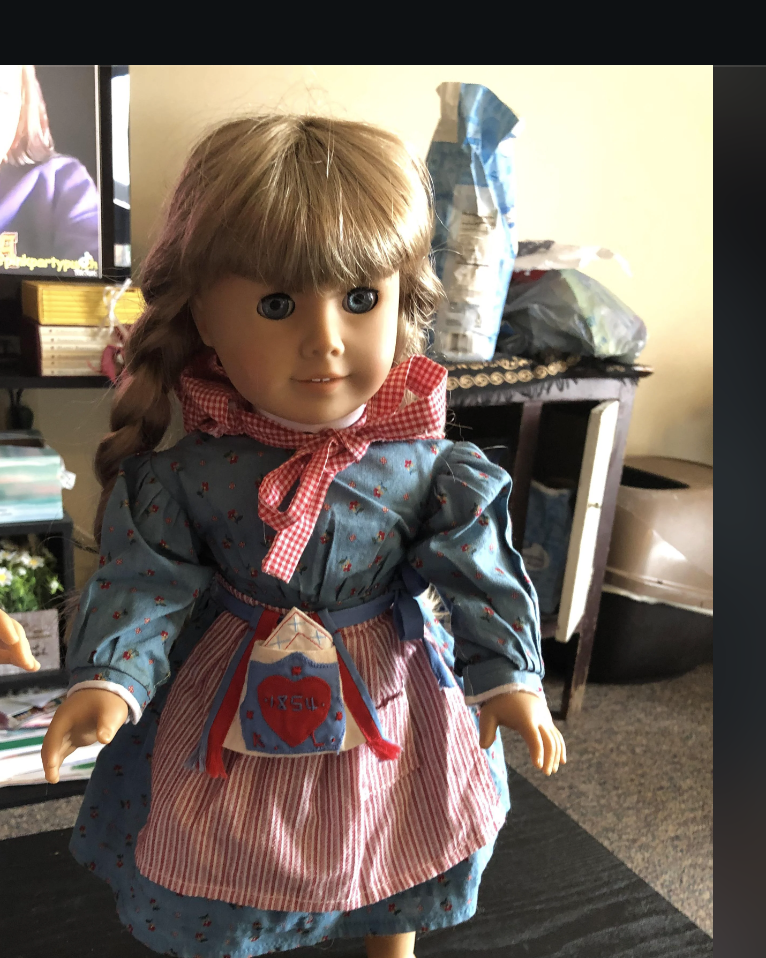 American Girl dolls Kirsten and Samantha stand on a table. Kirsten is missing shoes and socks, and Samantha is missing underwear, shoes, and socks