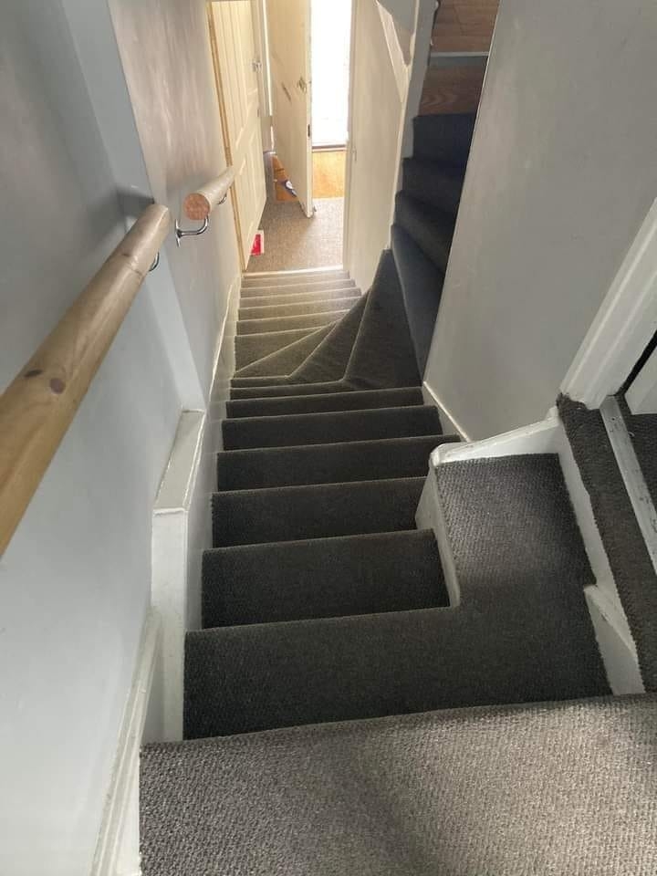 A gray-carpeted staircase with an awkward, irregular step near the bottom leading to a open door with light coming through