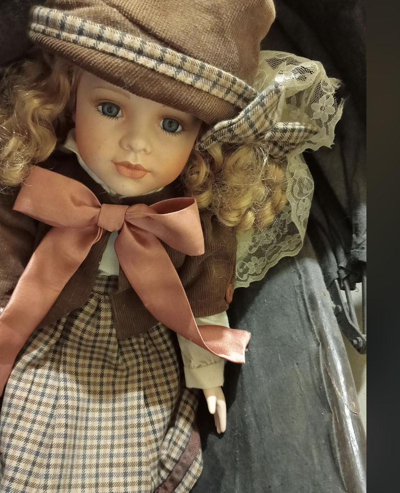 A porcelain doll with curly hair in a vintage outfit featuring a checkered hat and large ribbon. The Reddit post discusses people's favorite dolls and offers a poll