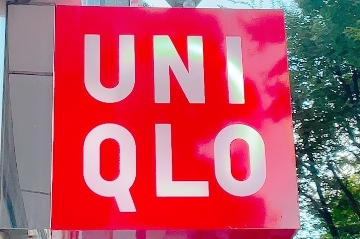 A red Uniqlo storefront sign with white letters, mounted on an outdoor building, surrounded by trees