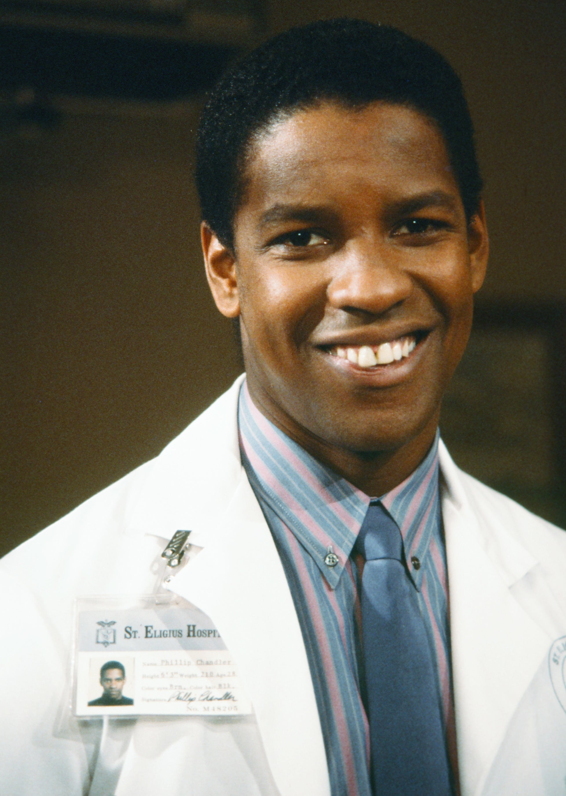 Denzel Washington smiling, wearing a white doctor's coat in a scene from "St. Elsewhere"