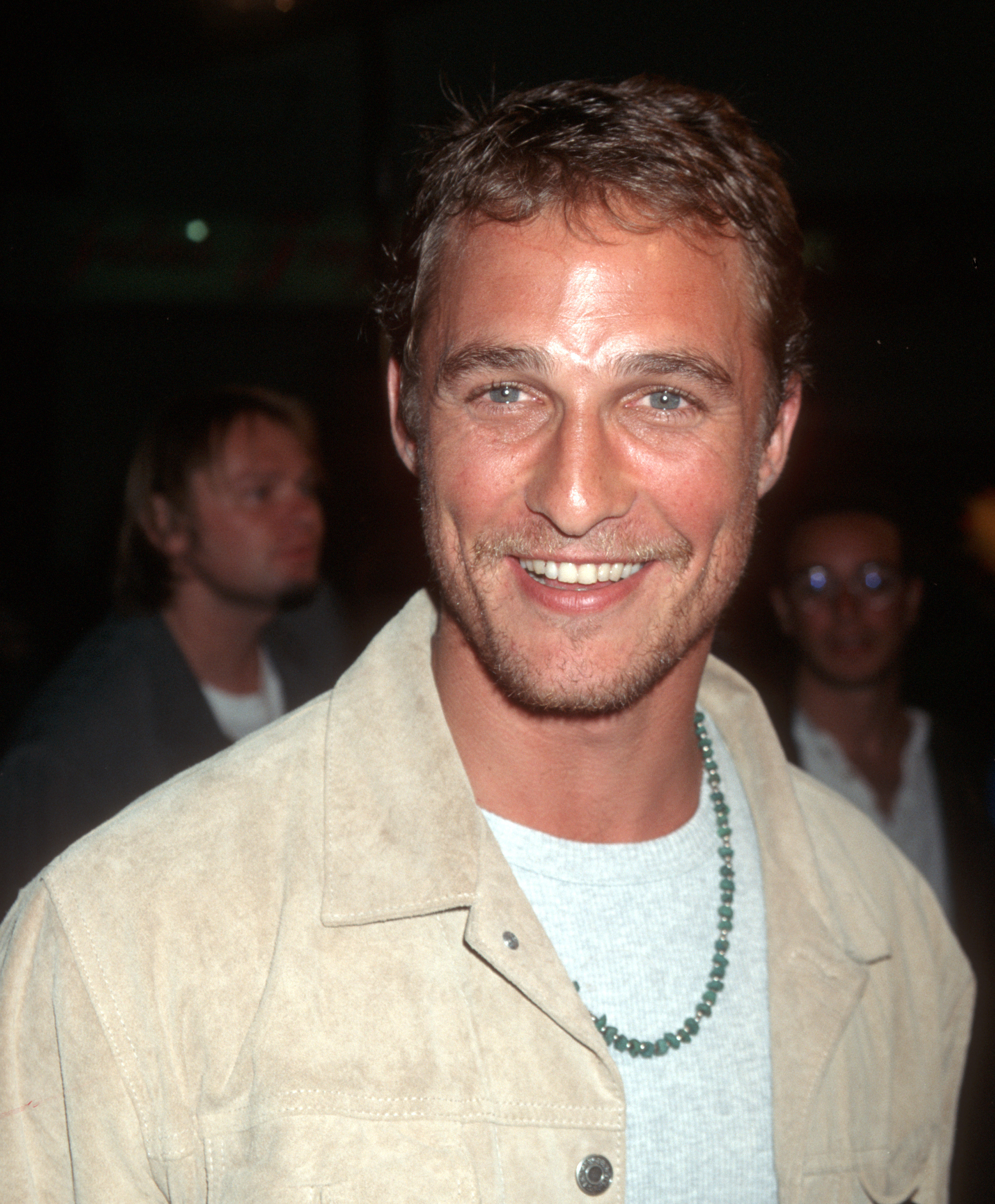 Matthew McConaughey smiling in a neutral jacket, and gray shirt