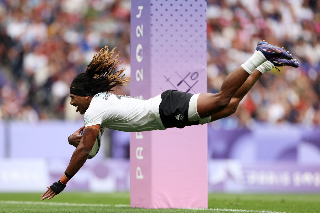 A rugby player with long hair dives to score a try at a match