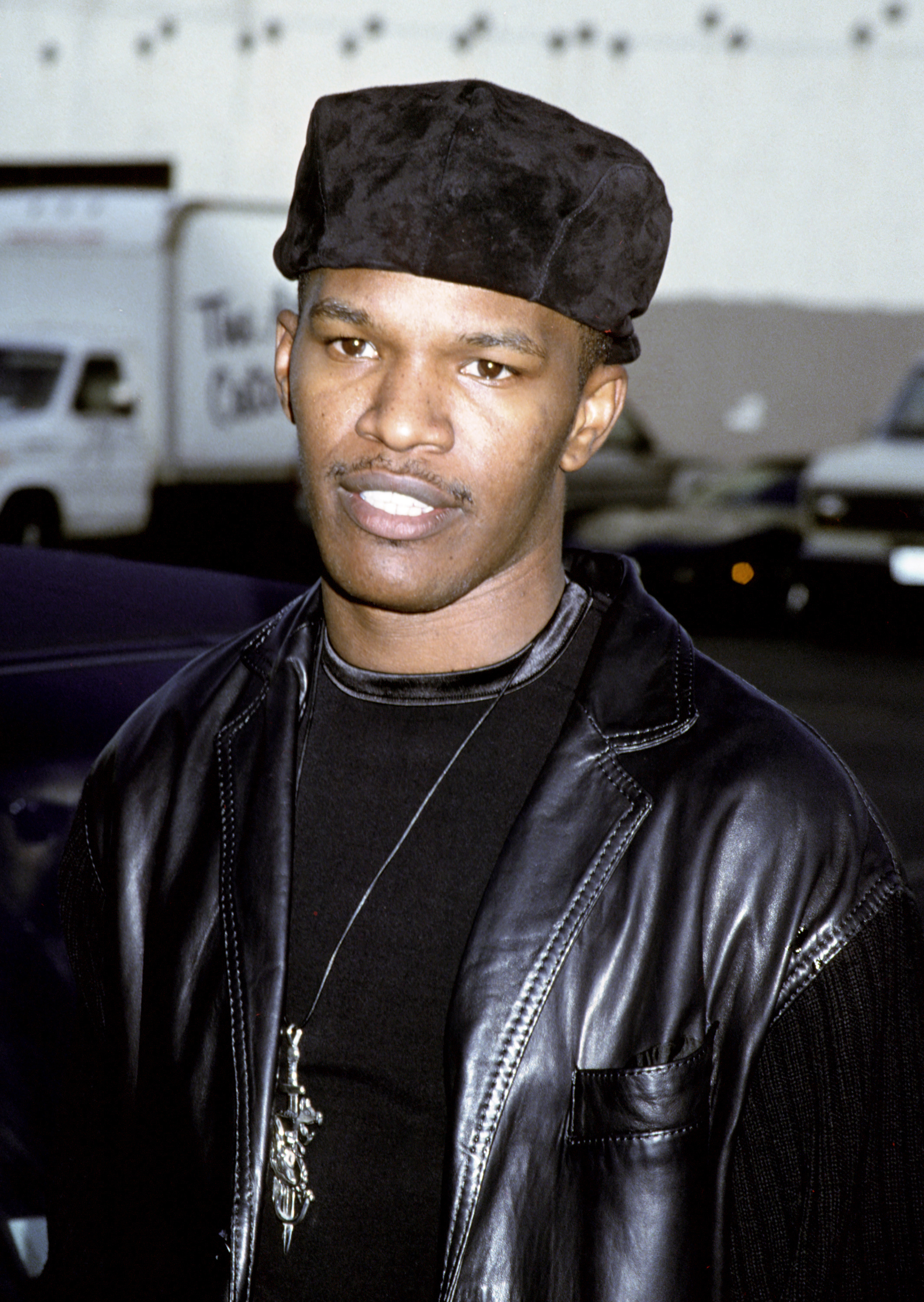 Jamie Foxx in a leather jacket and hat, standing outside