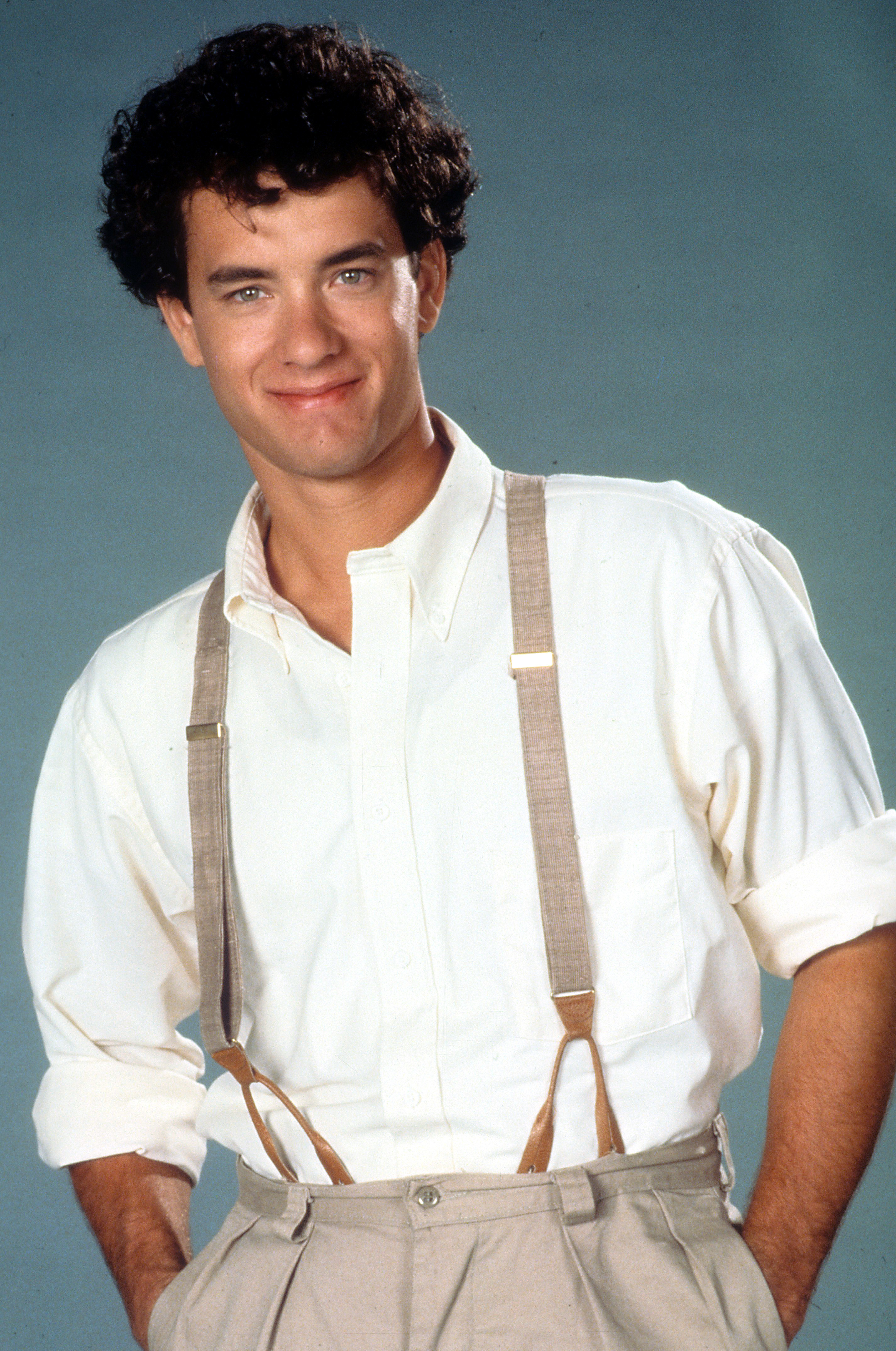 Tom Hanks smiles, wearing a white shirt with rolled-up sleeves and khaki suspenders