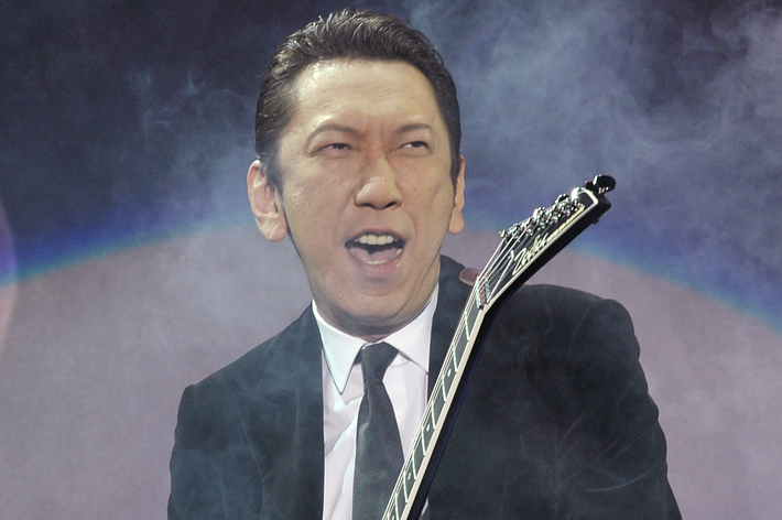 ギタリストの男性がスーツを着てエレキギターを演奏している姿。