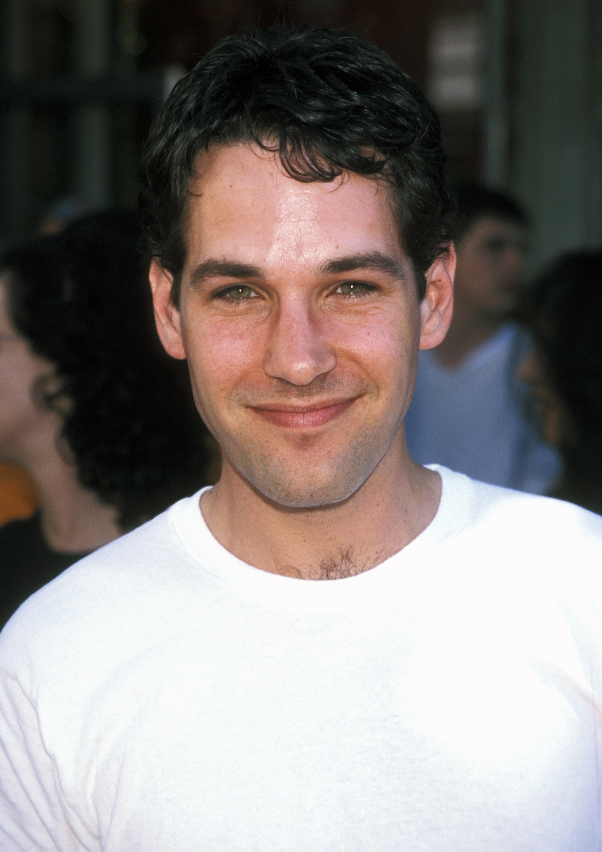 Paul Rudd smiles at the camera, wearing a plain white t-shirt, in an outdoor setting