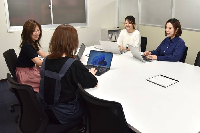 4人の女性がオフィスの会議室でノートパソコンを使用しながら会議をしている様子。