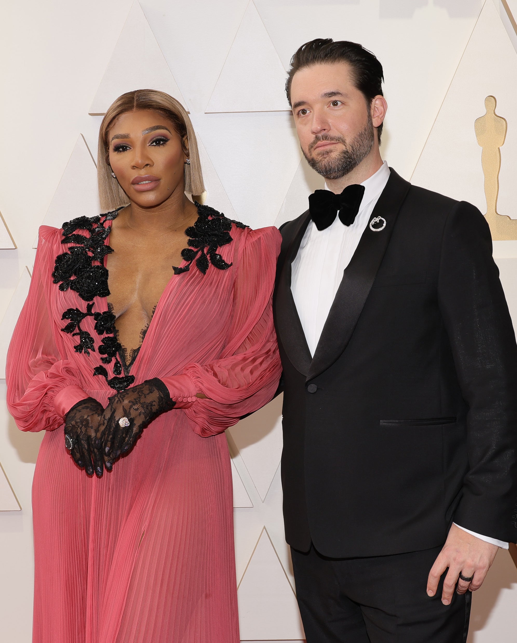 Serena Williams in a deep plunging pink dress with black floral details and Alexis Ohanian in a black tuxedo with a bow tie at an event