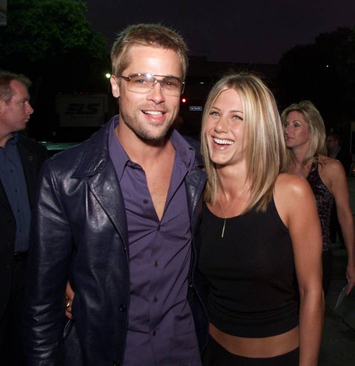 Brad Pitt in a leather jacket and Jennifer Aniston in a crop top, smiling together at an event