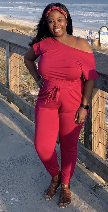 a reviewer successful an off-shoulder acheronian reddish jumpsuit, smiling connected a beachside boardwalk