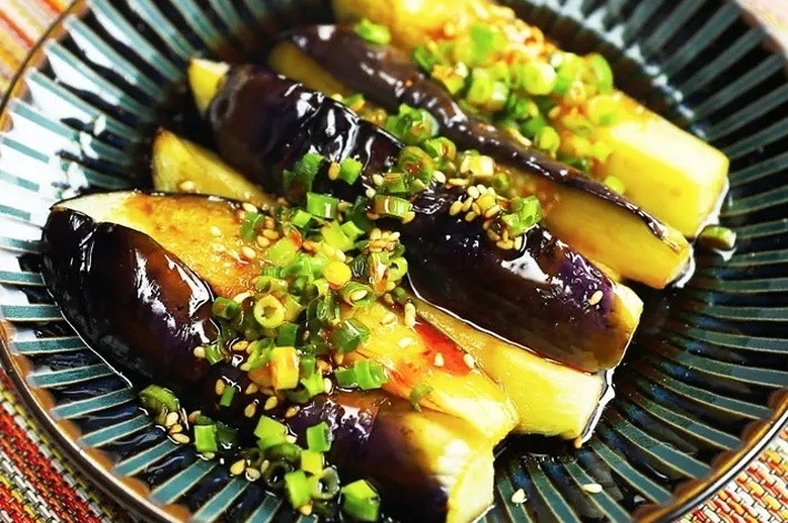 お皿に盛り付けられた茄子の料理。茄子にはネギと調味料がかかっており、美しく見せています。