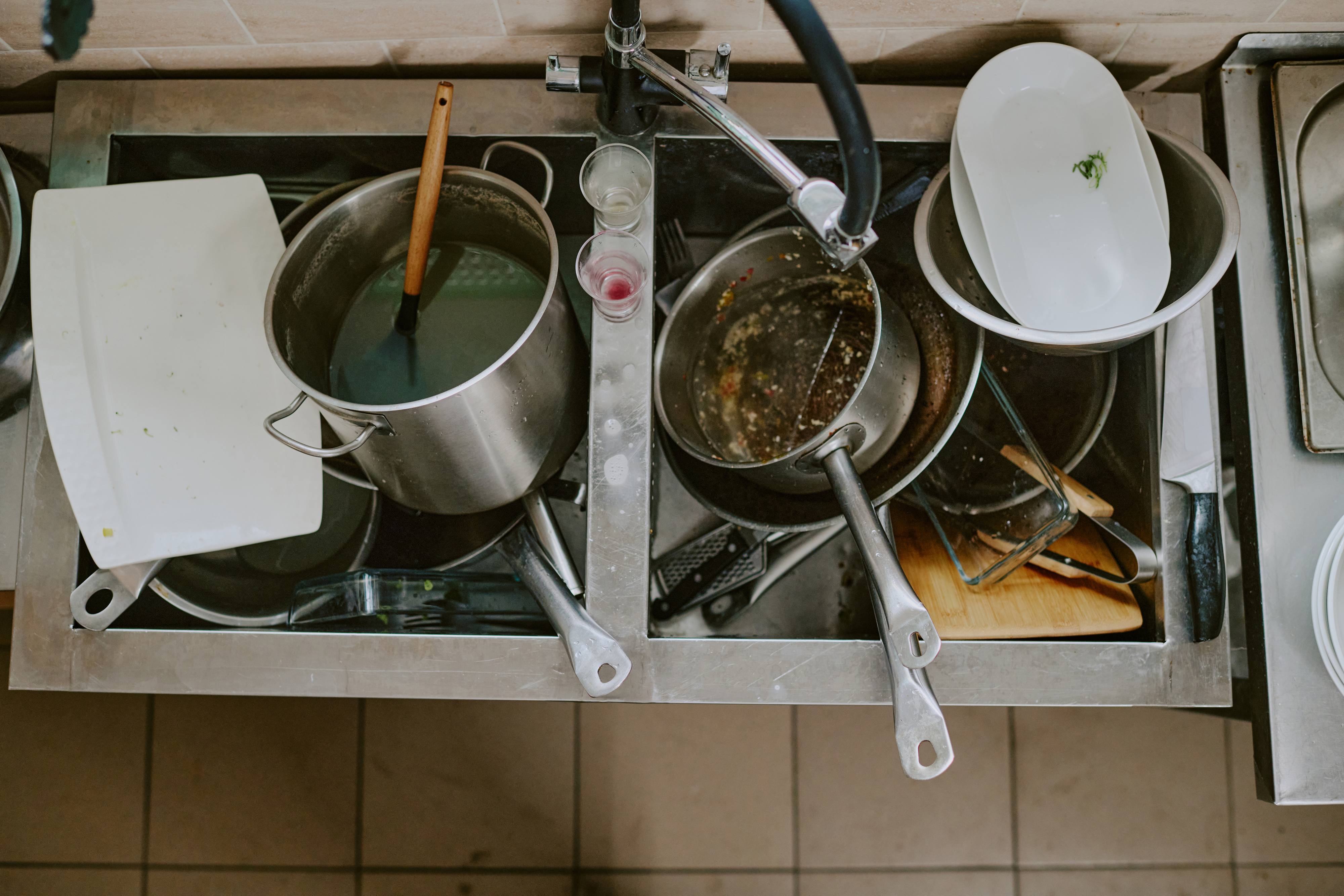 A messy kitchen sink filled with various dirty pots, pans, dishes, and cooking utensils