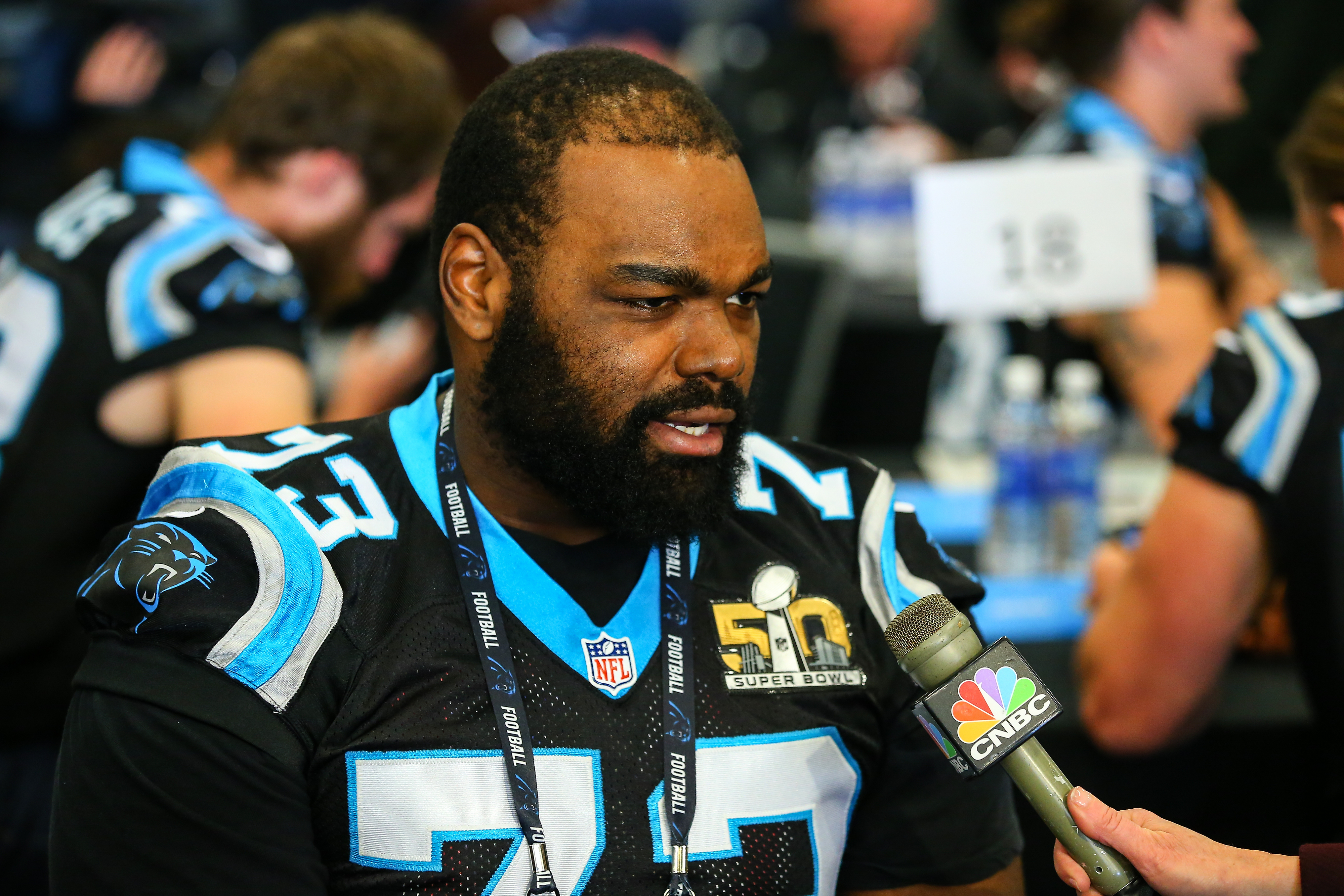 Michael Oher, wearing a Carolina Panthers jersey, is being interviewed by CNBC media at a Super Bowl 50 event