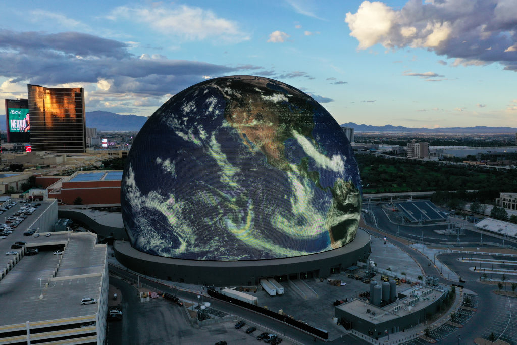 A large spherical building displays a digital image of Earth as seen from space. The surrounding area includes buildings, roads, and desert landscape