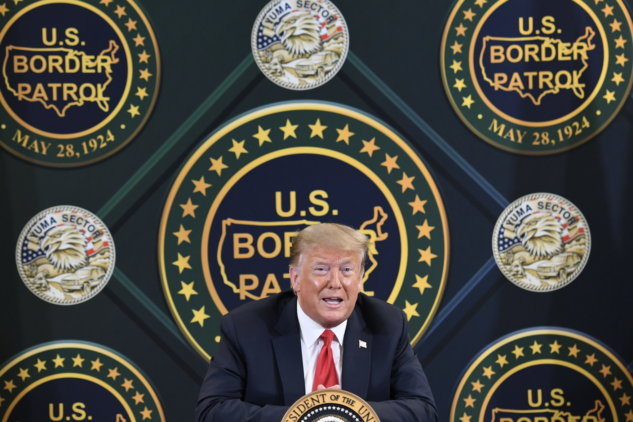 Donald Trump speaks at a podium with multiple U.S. Border Patrol insignias in the background