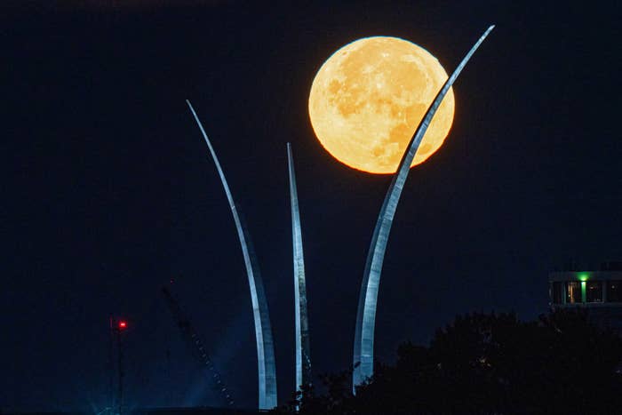 A large full moon rises behind three spires at night, creating a striking visual effect against the dark sky with silhouetted structures